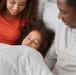 Parents of African descent watch their child go to sleep in bed.
