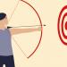 Archer aims a long bow and arrow at a bull's eye